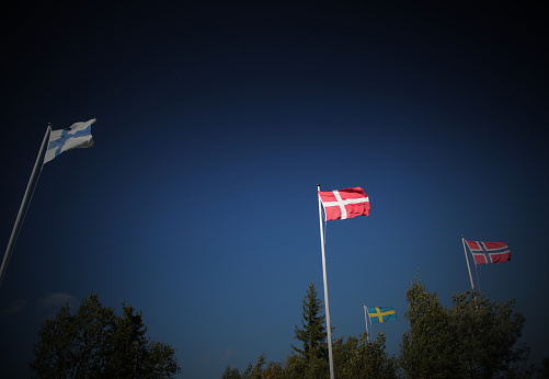 Flags of Finland, Denmark, Sweden and Norway blowing in the wind on dark blue sky. Vignetting was added.