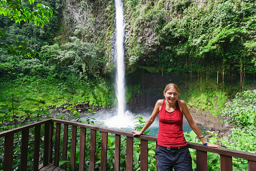 Young woman in front of waterfall in rainforest - Catarata Rio Fortuna, La Fortuna, Alajuela province, Costa Rica
