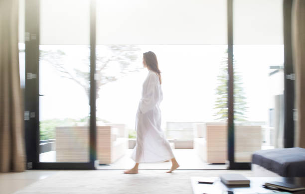 donna in accappatoio che cammina attraverso il soggiorno - full length windows foto e immagini stock