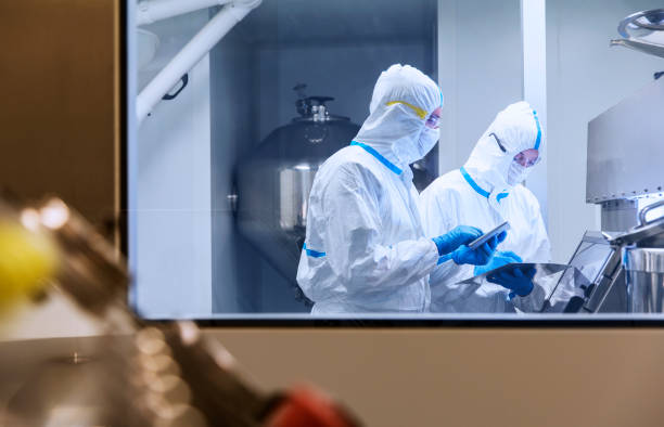 scientists in clean suits using digital tablets in experiment in laboratory - protective suit fotos imagens e fotografias de stock