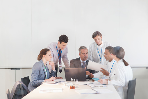 Happy business leader standing in a board room and looking at camera. There are people in the background.