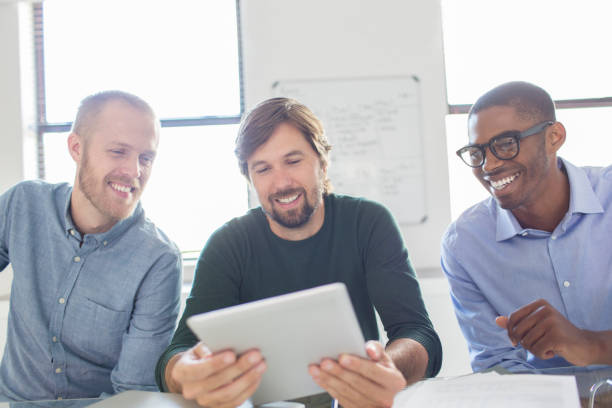 tres hombres sonrientes trabajando con tableta digital en la oficina - 24252 fotografías e imágenes de stock