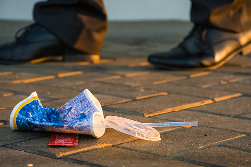 A soft-drink glass of Fast Food was thrown away the ground.  At its side a businessman walks quickly. Photo was taken on an autumn evening.