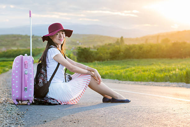 Lonely girl sitting on the road next to her suitcase