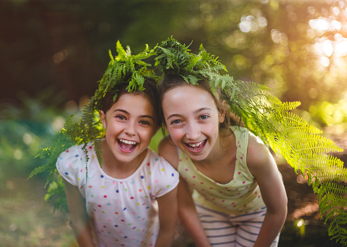 Two young girls wearing fern leaves on their heads laughing and smiling at camera.