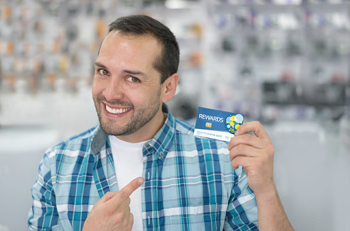 Man at a tech store holding a loyalty card to enjoy special benefits. Design on card is own design.