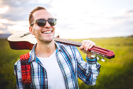 Photo of a young man with a guitar in the nature,background sunset.