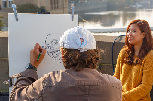 Prague, Czech Republic - October 6, 2014: Street artist paints a portrait-caricature of a beautiful girl on the Charles Bridge. Shallow depth of field, focus on the portrait