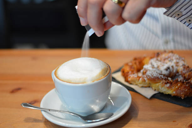 istock Hand pouring sugar into hot cappuccino 525495821