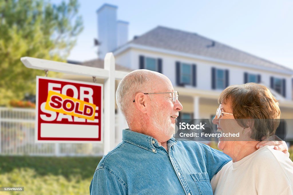 Senior Couple in Front of Sold Real Estate Sign, House Happy Affectionate Senior Couple Hugging in Front of Sold Real Estate Sign and House. Senior Adult Stock Photo