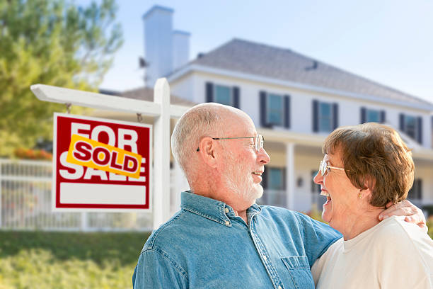 Senior Couple in Front of Sold Real Estate Sign, House Happy Affectionate Senior Couple Hugging in Front of Sold Real Estate Sign and House. house for sale by owner stock pictures, royalty-free photos & images
