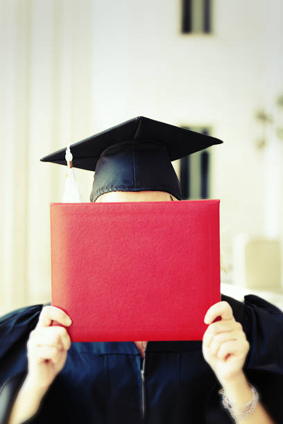 A graduating student holding up and reading the diploma in graduating ceremony