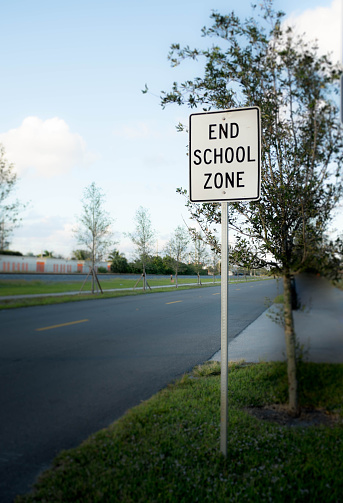 This photograph is of a white sign that signals the end of the school zone which means the traffic can resume at normal speeds.