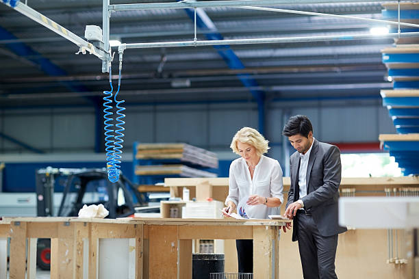 Workers looking at paperwork in factory Young businessman and senior female manager looking at paperwork in factory warehouse office stock pictures, royalty-free photos & images