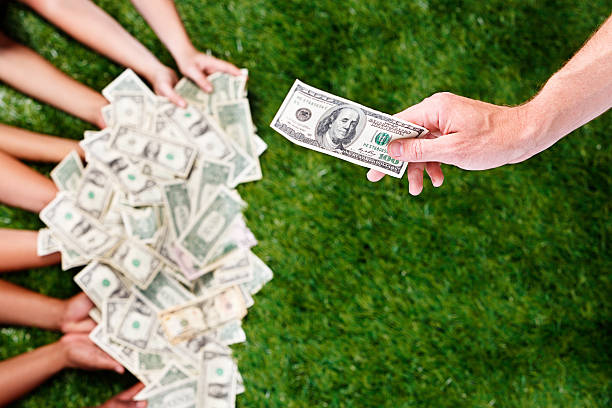 Many hands hold many US banknotes as another hand holds out yet another banknote. It's a windfall! The banknotes are unfocused to prevent reproduction.