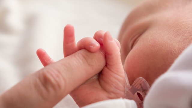 Newborn baby squeezes parents finger