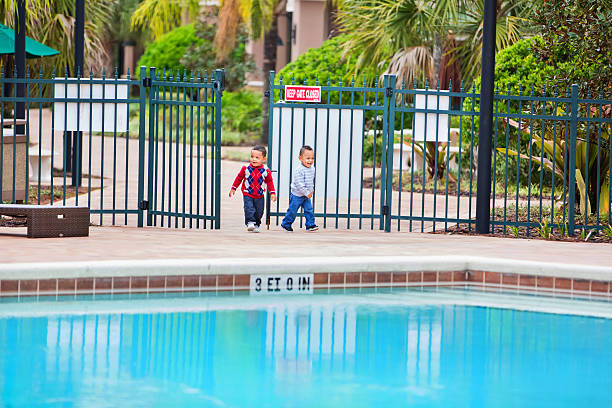 Toddler boys enter an unlocked gate at large unattended pool Two toddler boys are entering an unlocked gate at a large swimming pool at a resort.. There is no lifeguard on duty and no other people nearby. Shot with Canon 5D Mark 3 rr pool gate stock pictures, royalty-free photos & images