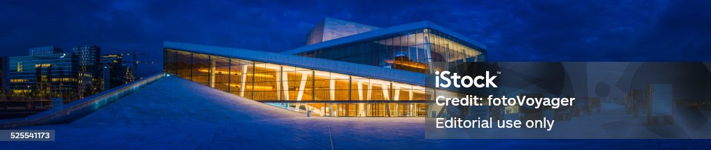 Futuristic opera house concert hall illuminated at dusk Oslo Norway Oslo, Norway - 13th July 2014: Deep blue dusk skies over the white slopes and warm glow of Oslo's Opera House and the futuristic skyscrapers of the Barcode Project development beside the tranquil waters of Oslofjorden, Norway. Composite panoramic image created from twelve contemporaneous sequential photographs.  Blue Stock Photo