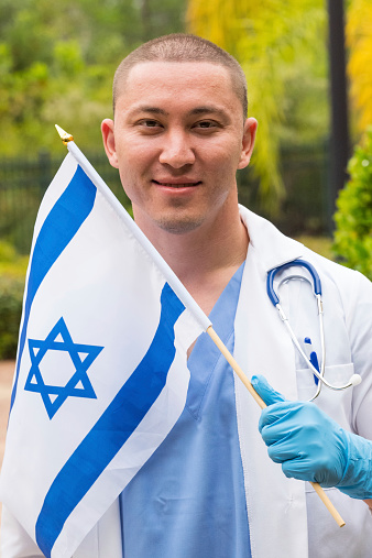 Smiling doctor looking at the camera holding an Israeli flag