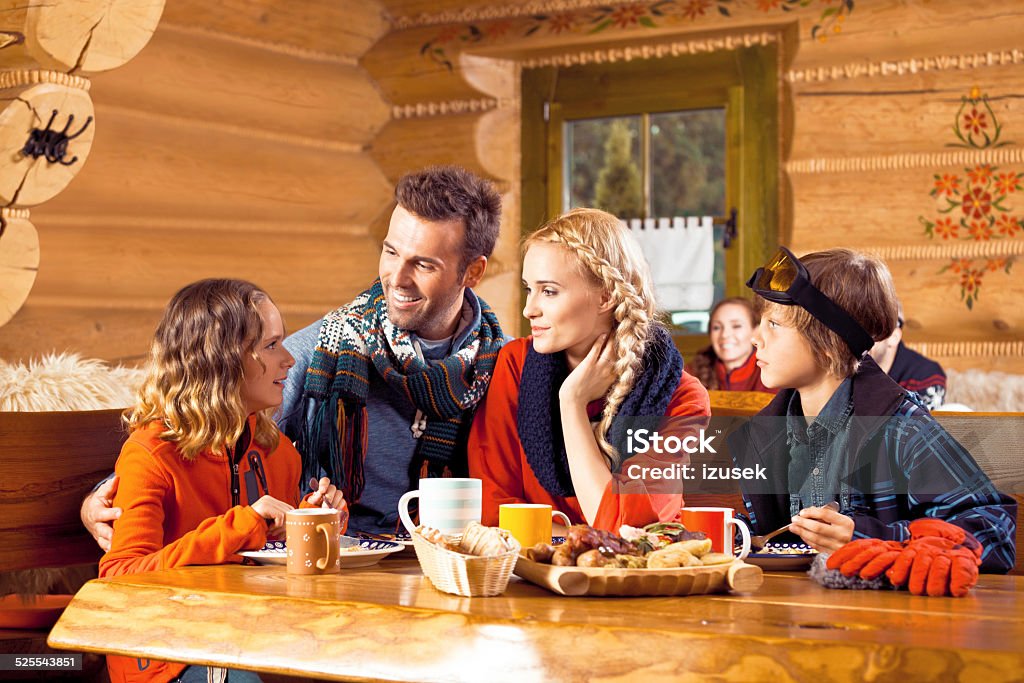 Family having lunch in restaurant after skiing Mother, father and their children wearing winter clothes sitting in a mountain restaurant after skiing, talking and enjoying dinner. Apres-Ski Stock Photo