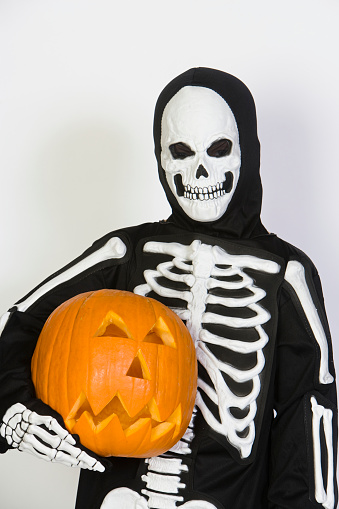Preadolescent boy in skeleton outfit holding pumpkin isolated over white background