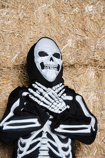 Preadolescent boy in skeleton outfit in front of stacked straw