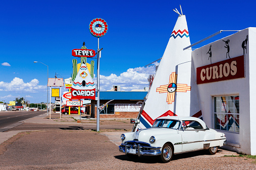 Tucumcari, United States - August 2, 2013: Old white fashioned car parked in front of a shop along the route 66. Several gift shops in the background