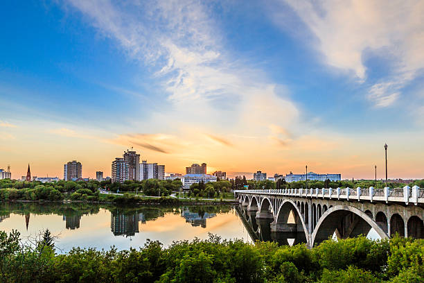A warm summer sunset over the city of Saskatoon located in Central Canada where the calm waters of the South Saskatchewan River flows under the University Bridge.
