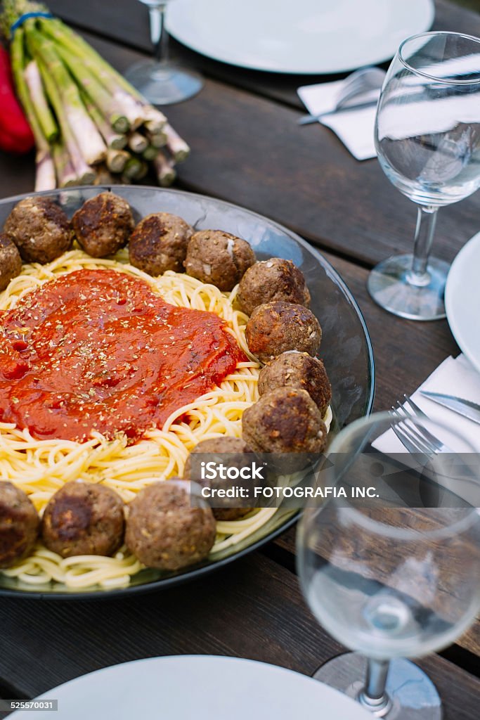 Spaghetti with Meatballs Summer lunch on the deck. Bowl of fresh cooked Pasta Spaghetti with tomato sauce, served with circle of Beef Meat balls. Outdoor table is set with plates, cutlery and glasses. Basil Stock Photo
