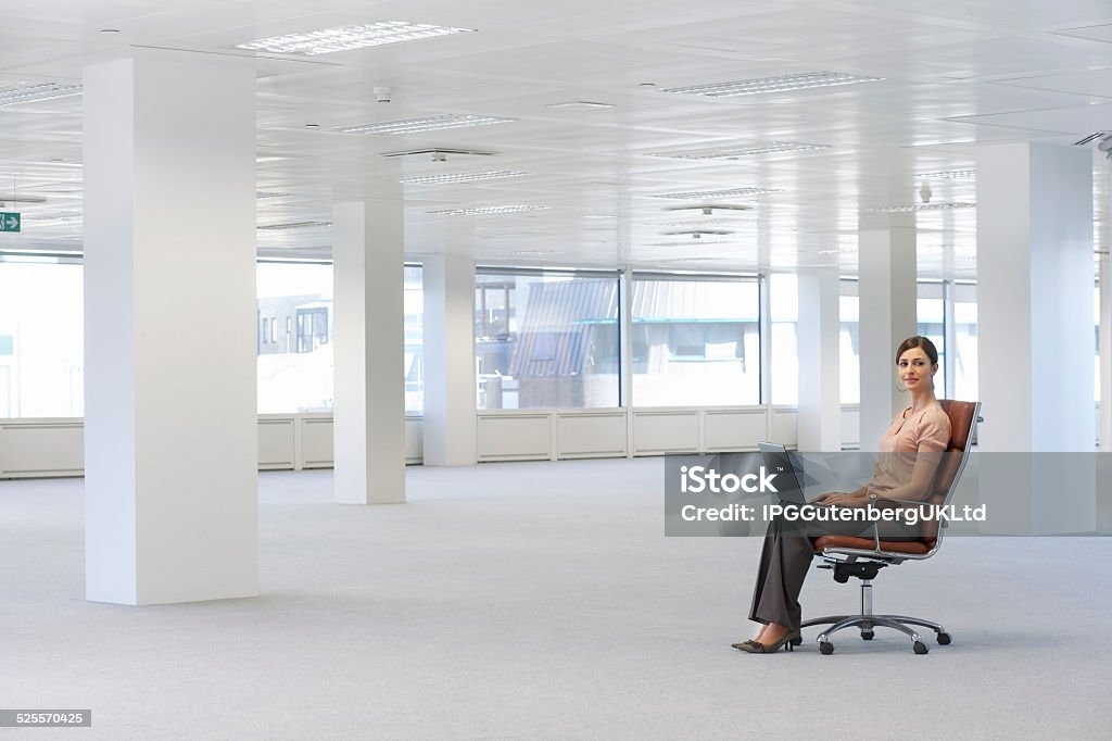 Businesswoman Using Laptop On Chair In Office Full length portrait of young businesswoman using laptop on chair in empty office space Adult Stock Photo