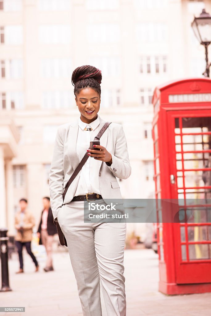 smart uk office worker a smart young female office worker walking through a uk business district whilst smiling at her smartphone. There is a british red phone box behind her and old fashioned lamppost . Red Telephone Box Stock Photo