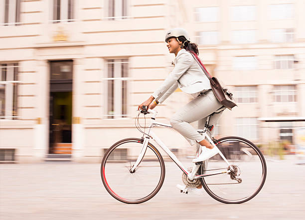cycling businesswoman commuter a young businesswoman or office worker is cycling through the business district in a trouser suit and a helmet. liverpool one stock pictures, royalty-free photos & images