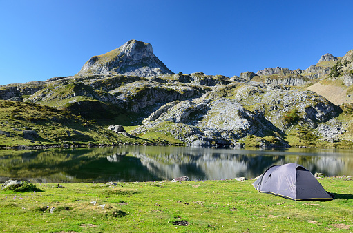 The tent is on the green shore of the alpine lake in the Atlantic Pyrenees﻿.