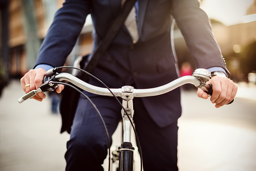 Close-up of businessman's hands holding the handle-bar of his bicycle in a urban area. Backlit shot.
