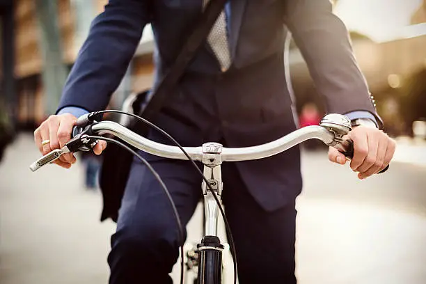 Close-up of businessman's hands holding the handle-bar of his bicycle in a urban area. Backlit shot.