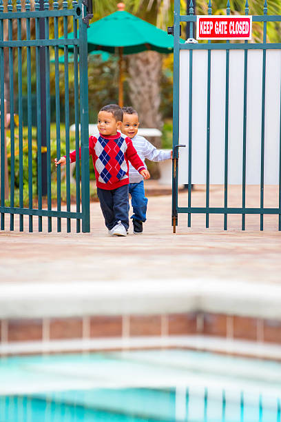 Terrible two's!. Twin boys get into a gate to pool Terrible two's times two! Two year old afro american twin boys have gotten through a closed gate to a swimming pool. Shot taken with a Canon 5D Mark 3 camera. RM pool gate stock pictures, royalty-free photos & images