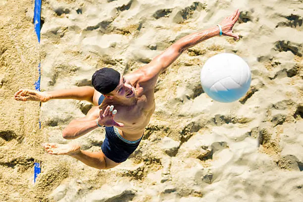 Top view of young male beach volley player serving the ball