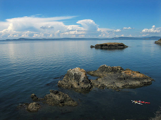 View across Puget Sound from Rosario Beach State Park.  In the foreground are rocky islands and two kayaks, the Olympic mountains are visible on the horizon.