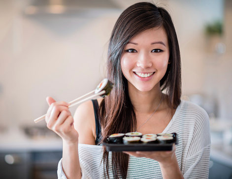 Happy Asian woman eating sushi with chopsticks