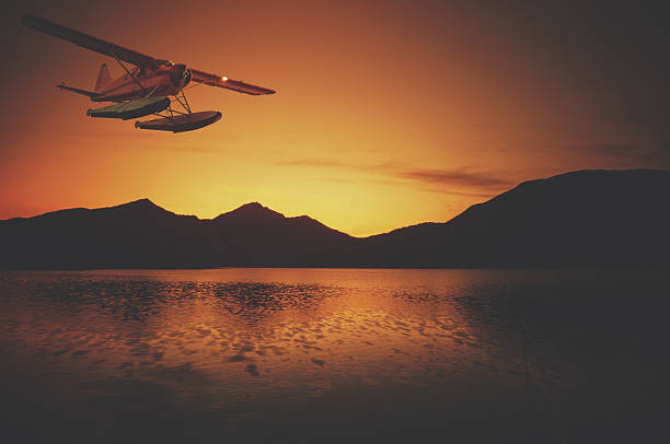 Bush Plane in Sunset A float plane flies in dusk light over mountains in Southern Alaska. bush plane stock pictures, royalty-free photos & images