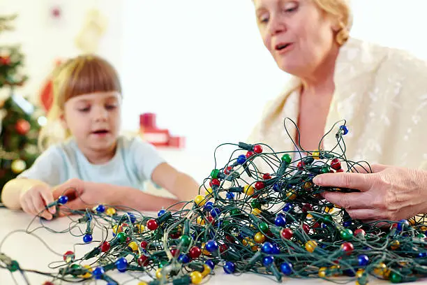 Senior woman and her little granddaughter untangling Christmas lights