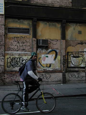 New York City, NY, USA - November 20, 2002: Man on a bike slows down to see why I'm taking a picture of a graffiti'd wall. 