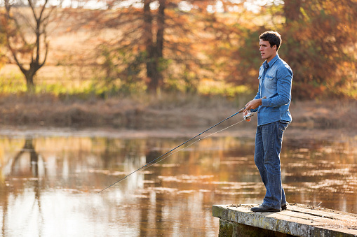 handsome young man fishing by a lake