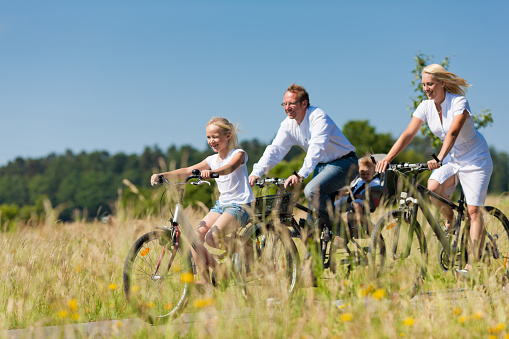 Family with baby and three girls having a weekend excursion on their bikes on a summer day in beautiful landscape