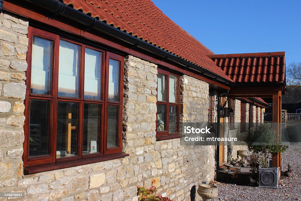 Image of old barn conversion house / bungalow, converted stables / outbuilding Photo showing a detached historic barn conversion house / bungalow.  These historic stables and outbuildings have recently been sympathetically converted into a luxury single storey dwelling, with new clay red roof tiles, wooden windows, a wood porch, restored and repointed brickwork, and some new stonework / cobblestone walls. Barn Stock Photo