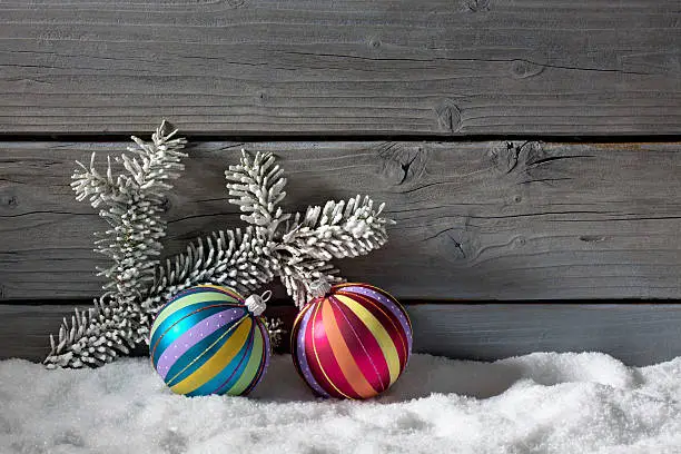 Colorful christmasballs on pile of snow against wooden wall.