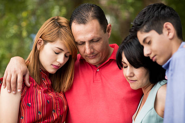 Front view of latin family praying with eyes closed A head and shoulders front view of an attractive latin family of four standing close and praying with eyes closed. face down stock pictures, royalty-free photos & images