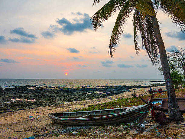 The view from Klong Hin beach, Koh Lanta, Krabi, Thailand, as the sun sets over the Andaman Sea.  An old long tail boat is onshore at low tide, beside a coconut tree or palm tree.