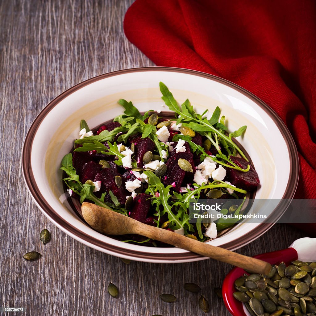 Beetroot salad with arugula, feta cheese and pumpkin seeds Beetroot salad with arugula, feta cheese and pumpkin seeds on a wooden background Appetizer Stock Photo