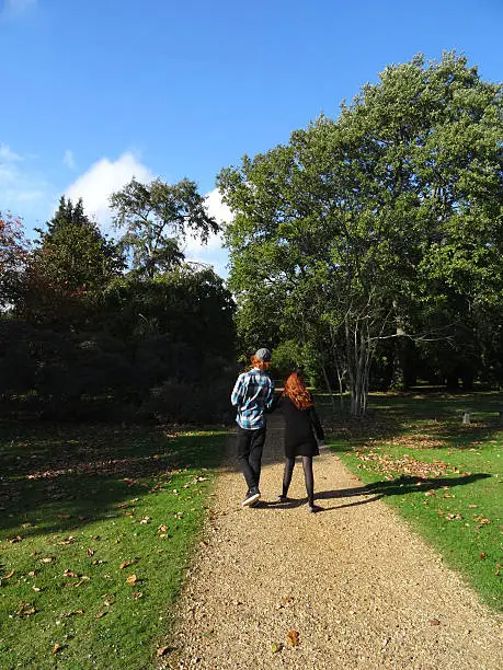 Photo showing a teenage boy and girl walking along woodland pathway / footpath, holding hands.  The boy and girl are actually brother and sister (siblings), messing around on a sunny afternoon.  They both have hair ginger / red hair and are pictured in the sunshine, with shadows from the surrounding trees falling on the path and lawn / grass.